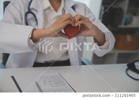 Hands of doctor woman holding red heart, showing symbol of love, human support to patient, promoting medical insurance, early checkup for healthcare, cardiologist help. Close up of object 111281405