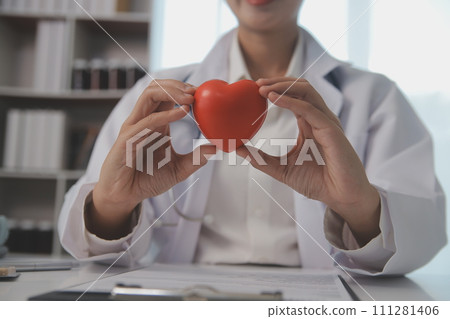 Hands of doctor woman holding red heart, showing symbol of love, human support to patient, promoting medical insurance, early checkup for healthcare, cardiologist help. Close up of object 111281406