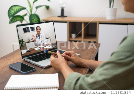 Patient engaging in a telemedicine session with a doctor on a laptop at home. 111281854