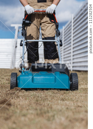 Scarifying lawn with scarifier, Man gardener scarifies the lawn and removal of old grass 111282504