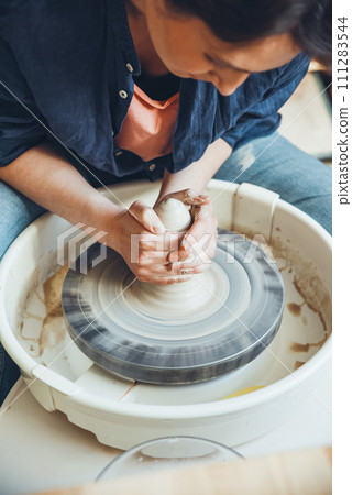 Pottery skill, a woman ceramist works on a potter's wheel. Female hands of a potter making a clay blank on a potter's wheel 111283544