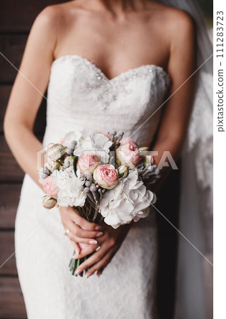 The bride in an elegant wedding dress holds a beautiful bouquet of different flowers and green leaves. Wedding theme 111283723