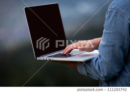 Man working outdoors with laptop in mountains. Concept of remote work or freelancer lifestyle. Cellular network broadband coverage. internet 5G. Man working outdoors with laptop in mountains. Concept of remote work or freelancer lifestyle. Cellular network broadband coverage. internet 5G. 111283742