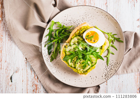 Close up of sandwich on ciabatta with avocado, cucumber, egg and arugula on a plate top view 111283806