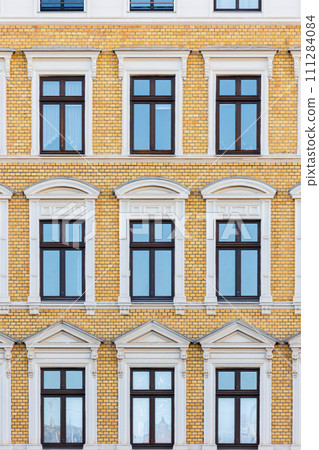 Elegant windows set facade vibrant yellow brick building, showcasing architectural symmetry and beautiful vintage windowsill stucco. Classic residential building front wall in european city center 111284084