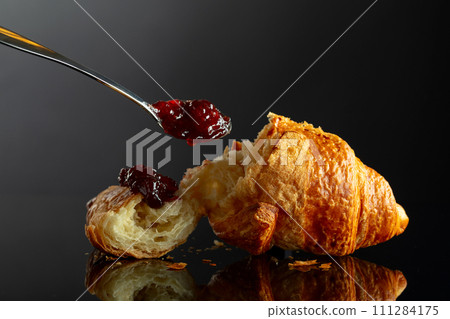 Fresh baked croissant with raspberry jam on a black background. 111284175