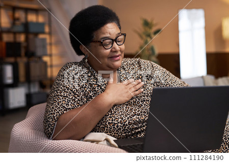 Portrait of smiling Black senior woman enjoying evening entertainment watching movies online via laptop copy space 111284190