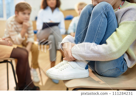 Close up of depressed young girl hugging knees and sharing mental health problem during support group for childrenwith copy space Close up of depressed young girl hugging knees and sharing mental health problem during support group for childrenwith copy space 111284231