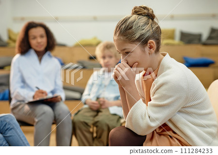 Side view portrait of depressed teen girl in support group meeting for childrenwith copy space Side view portrait of depressed teen girl in support group meeting for childrenwith copy space 111284233