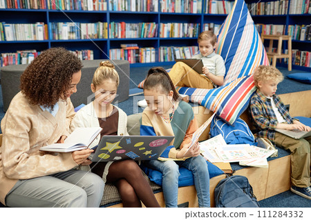 Portrait of two girls using laptop computer in modern library lounge with teacher helpingwith copy space 111284332