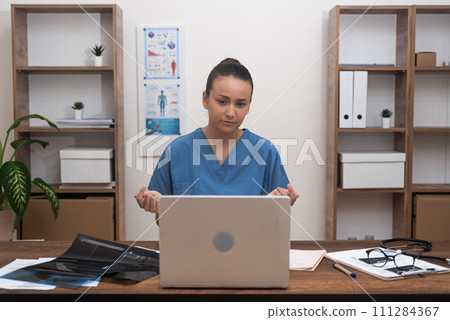 Telehealth Proficiency: The doctor, dressed in blue uniform, communicating with patient test results through her laptop during an online consultation, demonstrating telemedicine's role. Telehealth Proficiency: The doctor, dressed in blue uniform, communicating with patient test results through her laptop during an online consultation, demonstrating telemedicine's role. 111284367