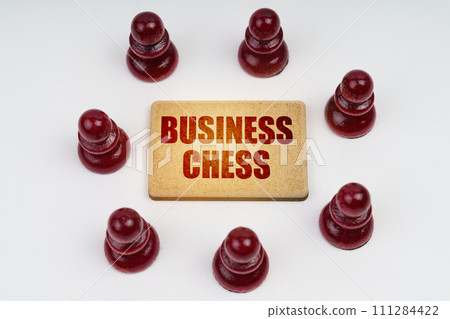On a white background, pawns stand around a sign with the inscription - Business Chess On a white background, pawns stand around a sign with the inscription - Business Chess 111284422