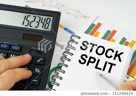 On the table there is a calculator, reports with graphs and a notepad with the inscription - Stock split On the table there is a calculator, reports with graphs and a notepad with the inscription - Stock split 111284424