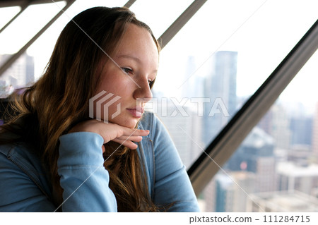 a young girl sits by the window, sad, lifts her chin with hand, looks into the distance without makeup, teen, adolescence, psychological experiences, first love, woman covers her eyes, thinks, dreams a young girl sits by the window, sad, lifts her chin with hand, looks into the distance without makeup, teen, adolescence, psychological experiences, first love, woman covers her eyes, thinks, dreams 111284715