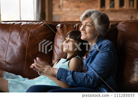 Happy preteen latina girl relax on couch in grandmother embraces 111285035