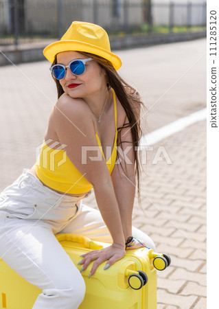 Conquest of new horizons: a stylish traveler in a yellow look feels excitement before the price. To new adventures: a girl in a stylish yellow look happily sits on a suitcase, ready to leave. Conquest of new horizons: a stylish traveler in a yellow look feels excitement before the price. To new adventures: a girl in a stylish yellow look happily sits on a suitcase, ready to leave. 111285120