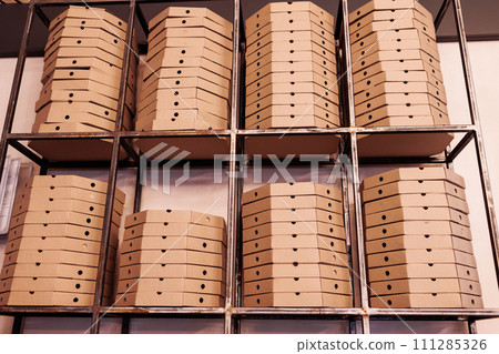 food delivery service. tall stacks of flat brown cardboard pizza boxes on metal shelf ready for delivery. craft packing boxes with pizza in stock in storage 111285326
