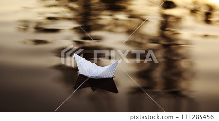 A paper boat is floating on the waves in the water at a beautiful sunset. Origami ship Sailing. The concept of a dream, future, childhood, freedom or hope. 111285456