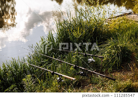 sunset fishing. fisher with spinning rod. Fisherman with rod, spinning reel on the river bank. Fishing for pike, perch, carp. wild nature. Article about fishing day. selective focus on fishing rod sunset fishing. fisher with spinning rod. Fisherman with rod, spinning reel on the river bank. Fishing for pike, perch, carp. wild nature. Article about fishing day. selective focus on fishing rod 111285547