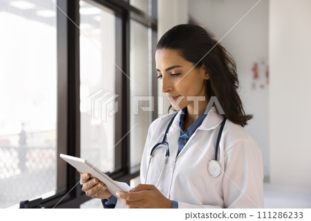 Serious young doctor woman using tablet for work 111286233