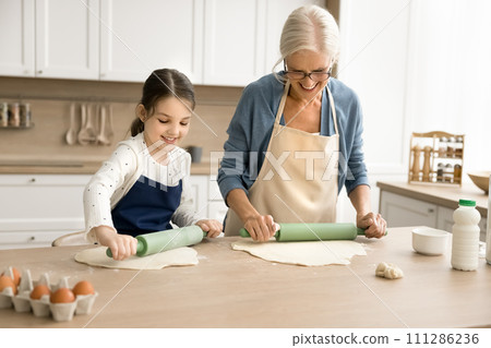 Sweet grandkid helping positive attractive grandma in apron to bake 111286236