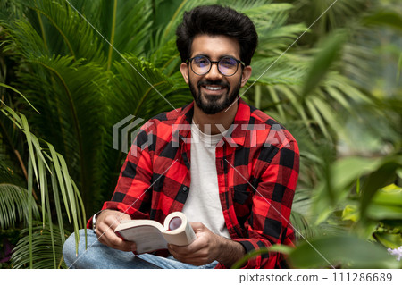 Hindu young man sitting in the garden with a book in hands 111286689