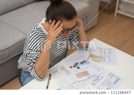 Debt-Stricken Distress: An unhappy woman, burdened by debt, grapples with managing household finances, calculating expenses, and making online payments. Debt-Stricken Distress: An unhappy woman, burdened by debt, grapples with managing household finances, calculating expenses, and making online payments. 111286847