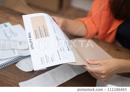 stern woman meticulously reviews utility bills, pondering rising costs of electricity, water, and internet services with deep concern 111286865