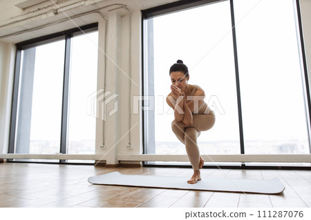 Lady balancing on one leg and keeping hands in namaste gesture at training room. 111287076