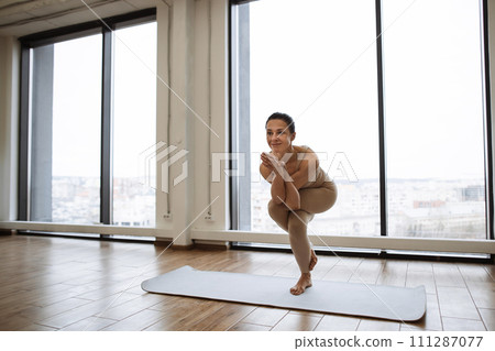 Lady balancing on one leg and keeping hands in namaste gesture at training room. 111287077
