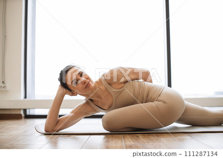 Brunette in sportswear smiling and looking at camera while lying on yoga mat. Brunette in sportswear smiling and looking at camera while lying on yoga mat. 111287134