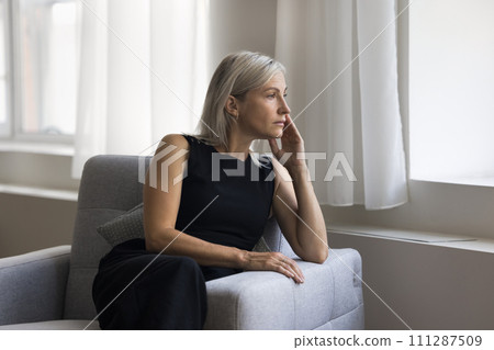 Attractive mature blonde woman relaxing alone seated on cozy armchair Attractive mature blonde woman relaxing alone seated on cozy armchair 111287509