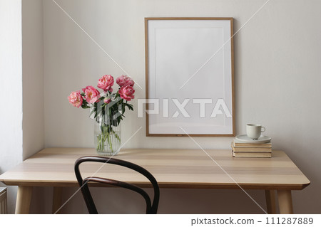 Elegant interior still life. Blank vertical picture frame mockup. Vase with pink peonies flowers. Cup of tea, coffee on books. Wooden table, desk. Romantic home breakfast. White wall background. Elegant interior still life. Blank vertical picture frame mockup. Vase with pink peonies flowers. Cup of tea, coffee on books. Wooden table, desk. Romantic home breakfast. White wall background. 111287889