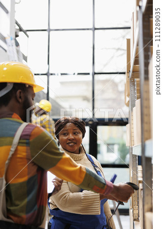 Warehouse supervisor coordinating employee trainee scanning goods packages. African american storehouse operators checking merchandise stock with barcode scanner equipment 111289035