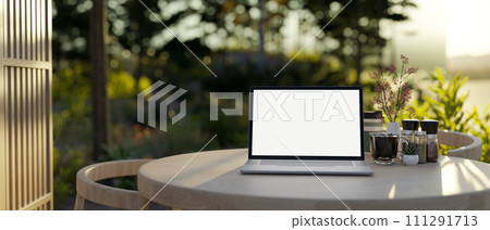 A laptop computer mockup on a wooden table on an outdoor patio lounge with a green garden. 111291713