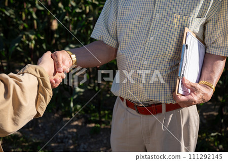 A senior male farmer is shaking hand with a female supplier or agronomist in his corn field. 111292145