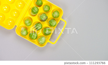 Raw organic Brussel sprouts in yellow container on grey background, top view. Flat lay, overhead, from above. Copy space. 111293766