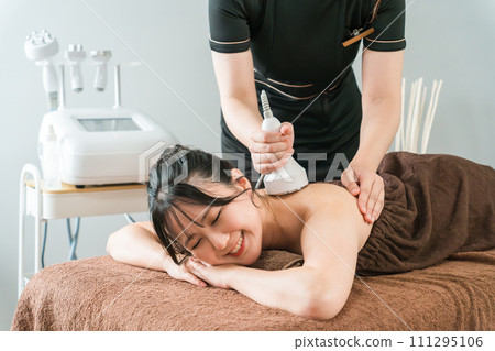 Esthetician and woman performing slimming beauty treatment using cavitation beauty machine at beauty salon 111295106