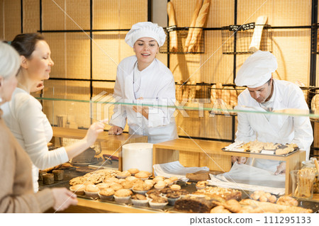Portrait of two male female bakery workers of different ages selling pastry to consumers in bakehouse Portrait of two male female bakery workers of different ages selling pastry to consumers in bakehouse 111295133