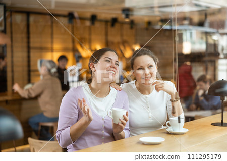 Carefree female colleagues drinking coffee and chatting in cafe 111295179