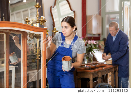 Young female furniture maker diligently working on vintage glass cabinet in workshop Young female furniture maker diligently working on vintage glass cabinet in workshop 111295180