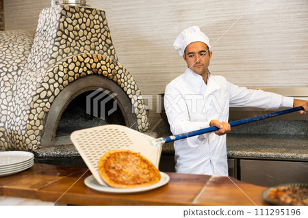 Chef holding big shovel with pizza in kitchen restaurant Chef holding big shovel with pizza in kitchen restaurant 111295196