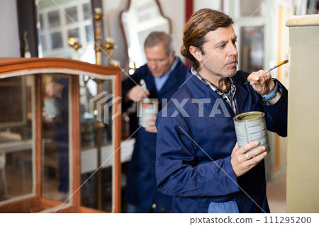 Male furniture maker diligently working on vintage glass cabinet in workshop 111295200