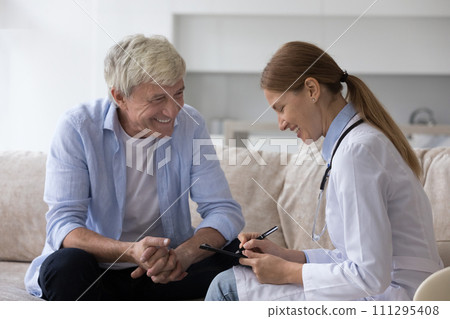 Positive elderly man consulting young doctor woman at home 111295408