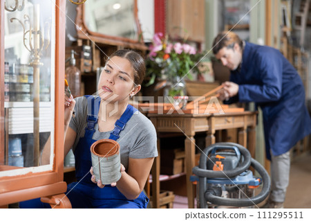 Young female furniture maker diligently working on vintage glass cabinet in workshop 111295511