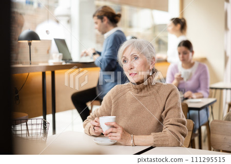 Elderly woman in casual clothes with mug of hot drinks, sipping tea or coffee at cafe table Elderly woman in casual clothes with mug of hot drinks, sipping tea or coffee at cafe table 111295515