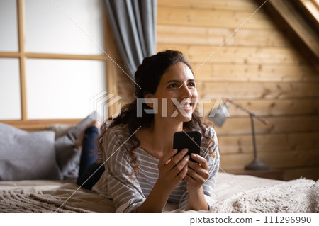 Dreamy young hispanic female lie on bed relax with smartphone Dreamy young hispanic female lie on bed relax with smartphone 111296990