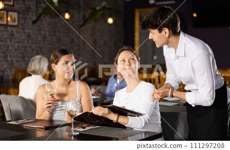 Young male waiter taking order from two women in restaurant 111297208