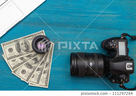 Earn money in internet DSLR camera, dollars, laptop, on blue wooden background, top view Earn money in internet DSLR camera, dollars, laptop, on blue wooden background, top view 111297284
