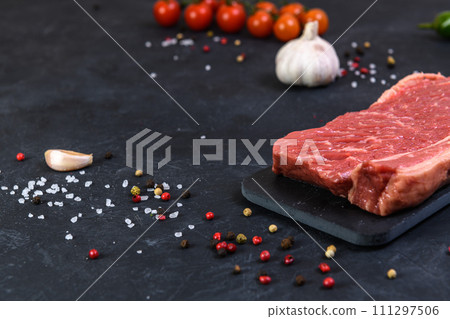 Raw fresh marbled meat and seasonings on dark background Raw fresh marbled meat and seasonings on dark background 111297506